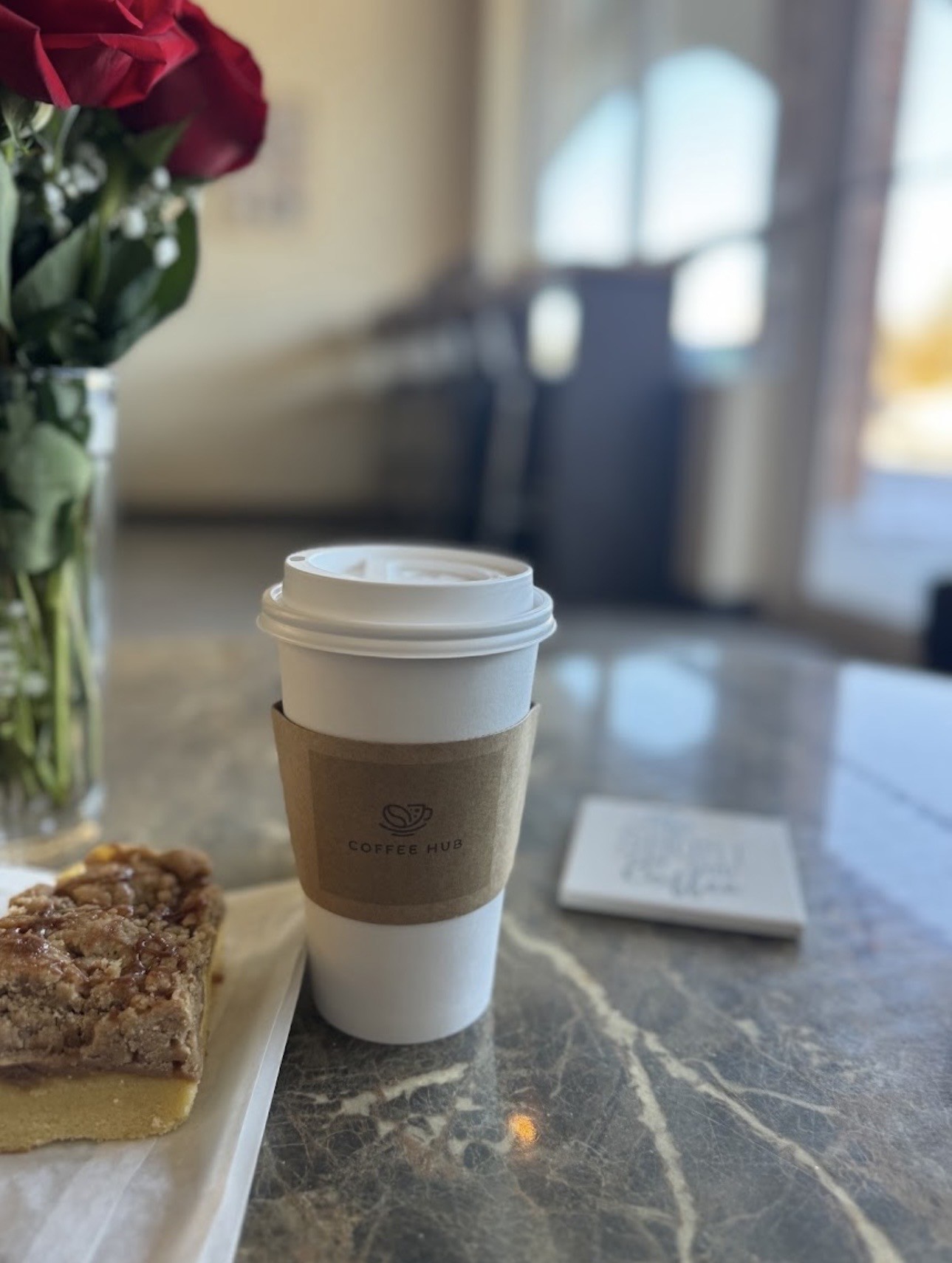 Coffee Hub takeaway coffee beside a pastry and red roses